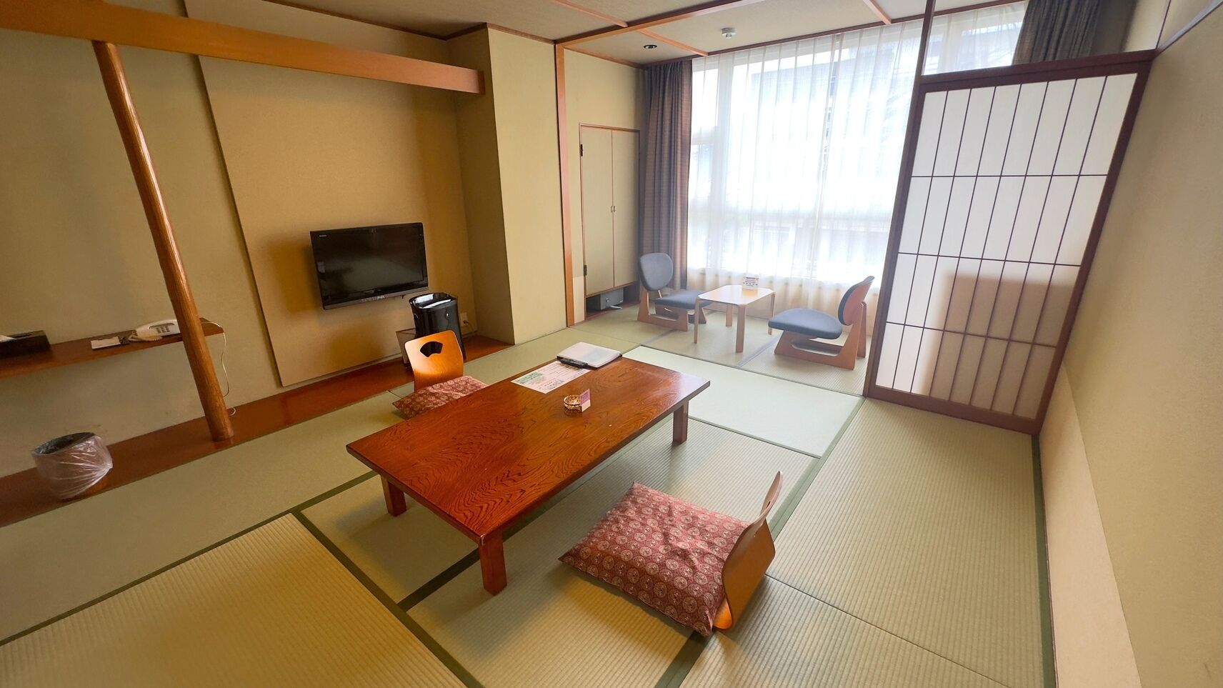 A traditional Japanese room with tatami flooring, a low table with cushions, a television, and sliding doors.