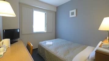 A hotel room with a bed, a desk with a telephone, a chair, a television, and a window with blinds.