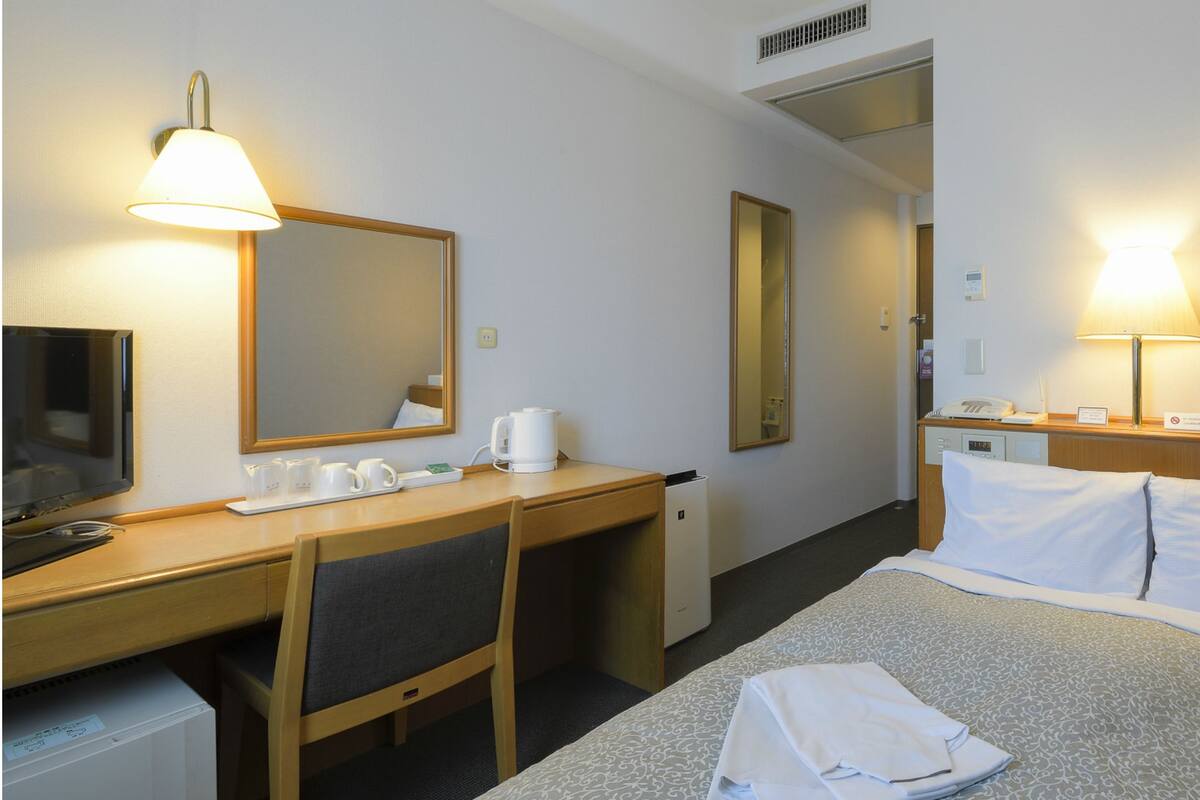 A hotel room with a bed, a desk with a chair, a television, and two lamps.