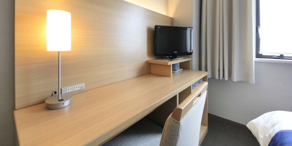A hotel room with a wooden desk, a television, a lamp, and a bed.