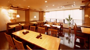 A restaurant with wooden tables and chairs, potted plants, and a view of the sea. - Shonandai Dai-Ichi Hotel Fujisawa Yokohama (Fujisawa)