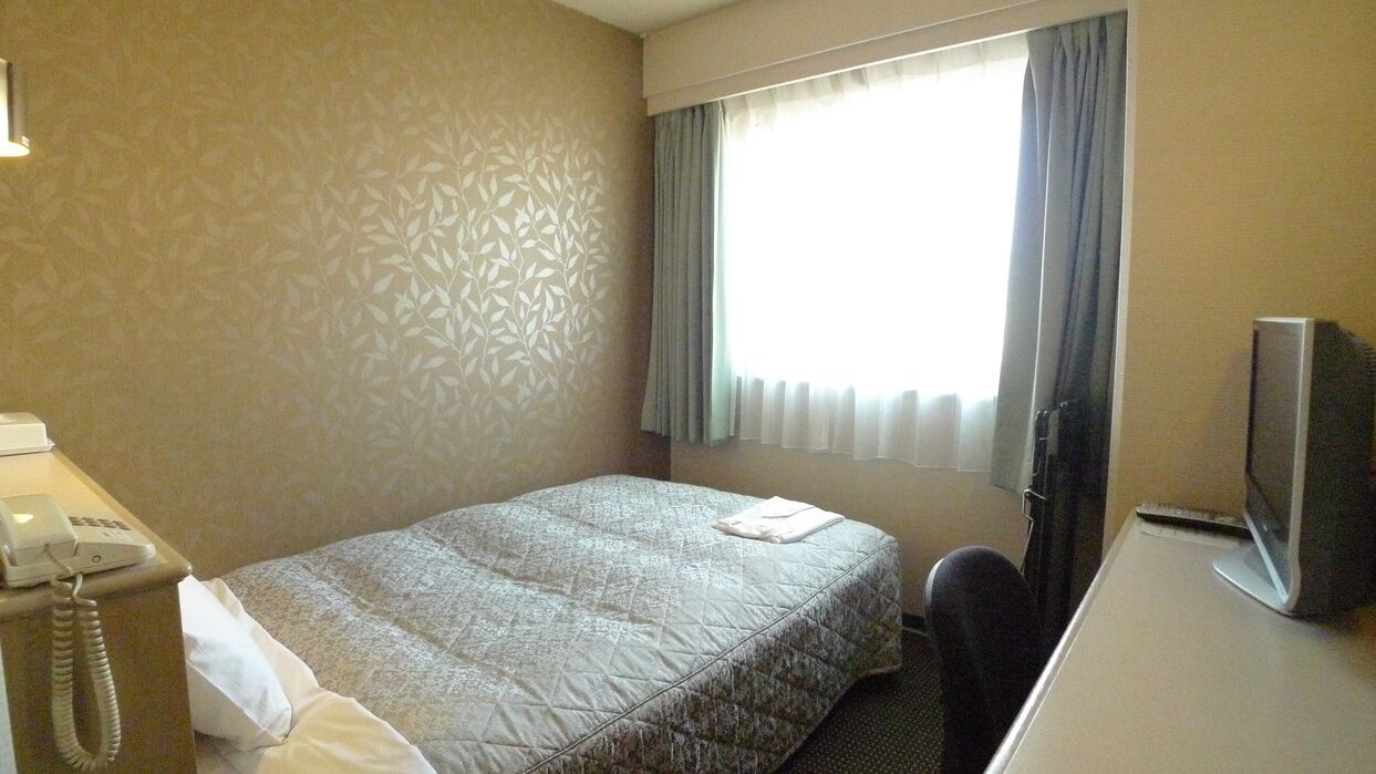 Ein Hotelzimmer mit Bett, Schreibtisch mit Computer, Telefon und einem Vorhangfenster.