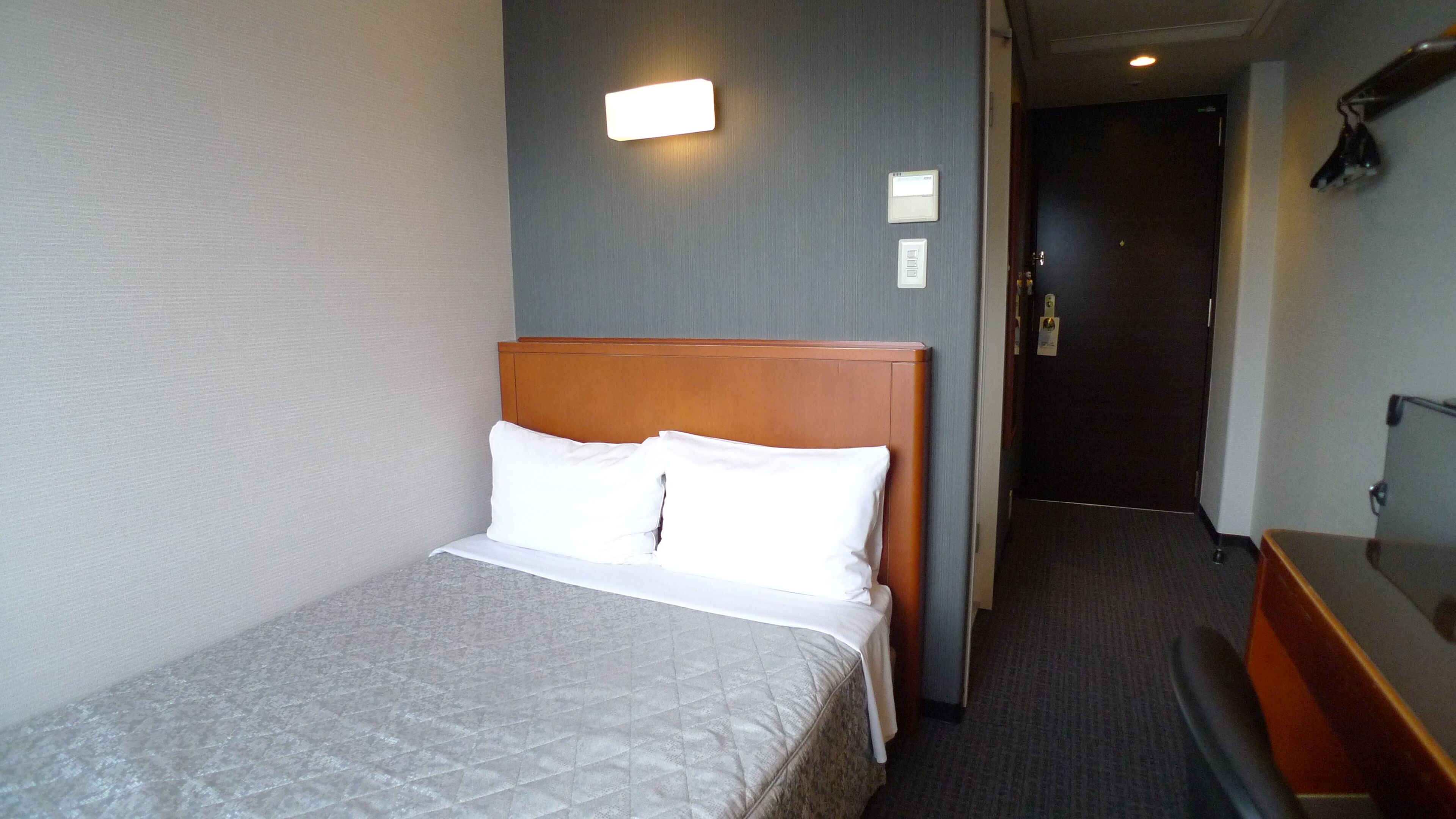 Ein Hotelzimmer mit Bett, Kopfteil, Wandleuchte und einer Tür zu einem anderen Raum.