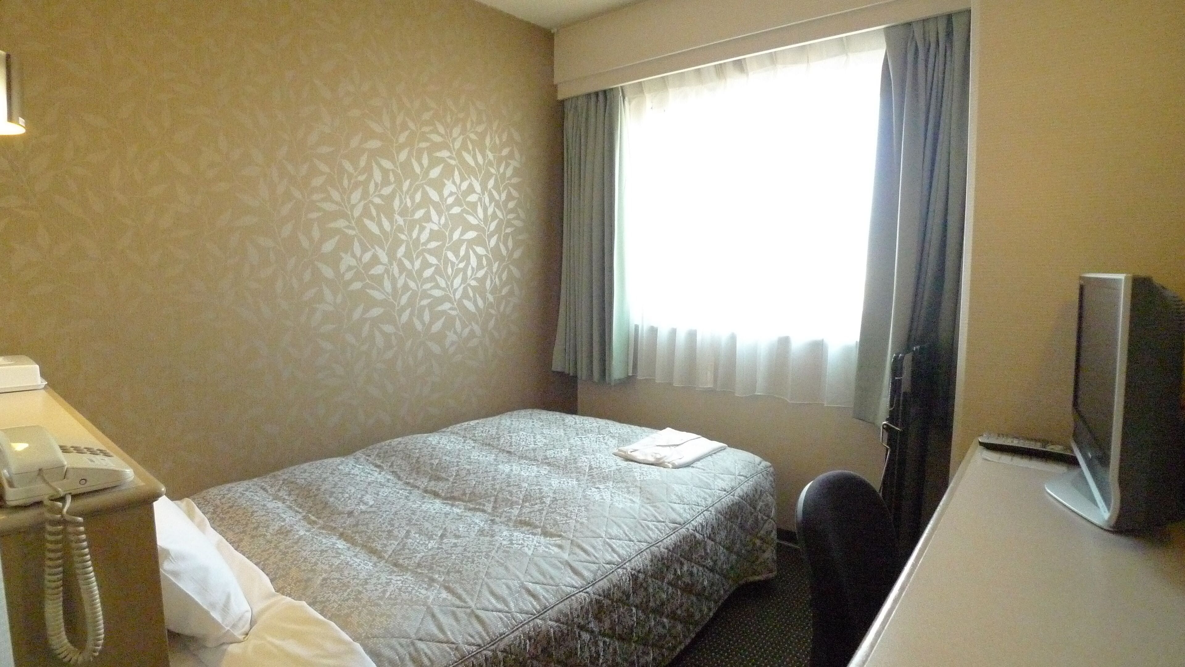 Ein Hotelzimmer mit Bett, Schreibtisch, Fernseher und Telefon.