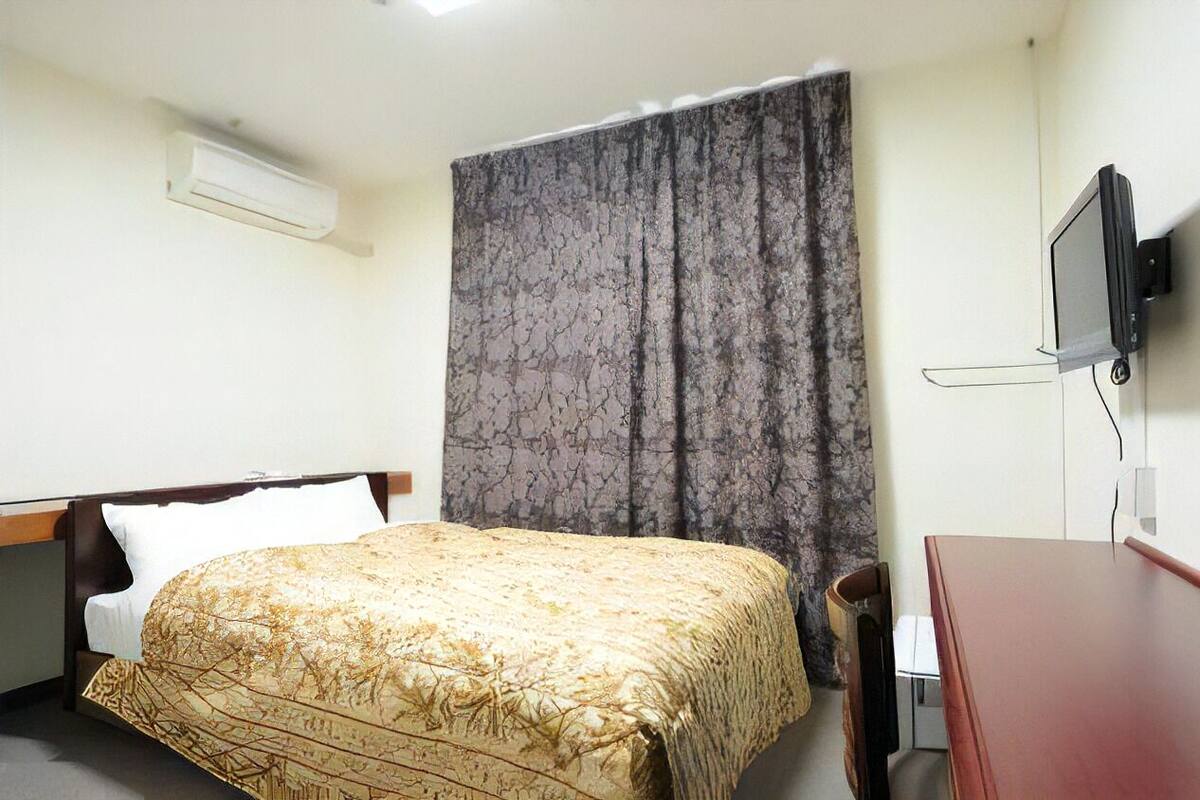 A hotel room with a bed, a desk, a television, and an air conditioning unit.