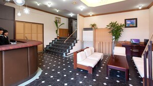 A hotel lobby with a reception desk, a sofa, a coffee table, and a staircase. - Beppu Ekimae Hotel Hayashi (Beppu)