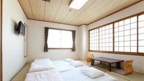 A traditional Japanese room with tatami flooring, a low wooden ceiling, a futon bed, a television, and a sliding door with a view of the outside. - Beppu Ekimae Hotel Hayashi (Beppu)