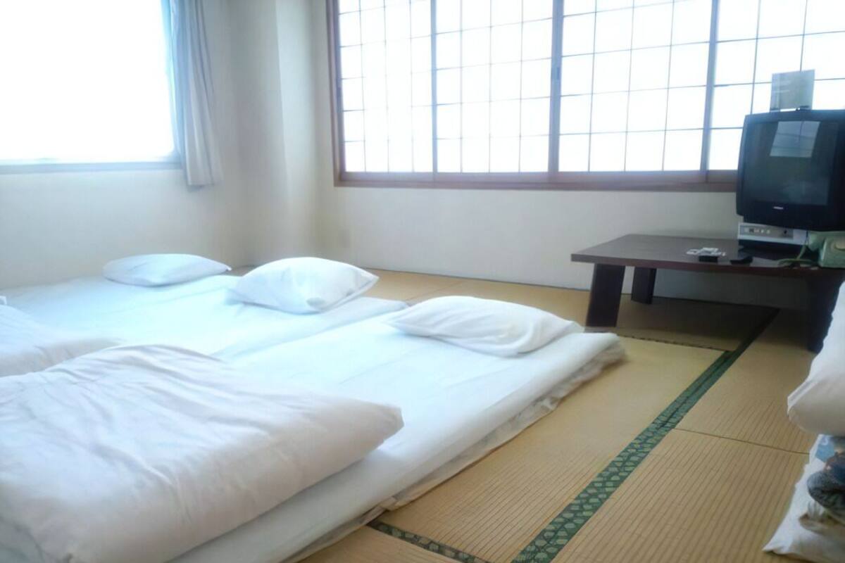 A hotel room with two beds, a television, and a window with blinds.