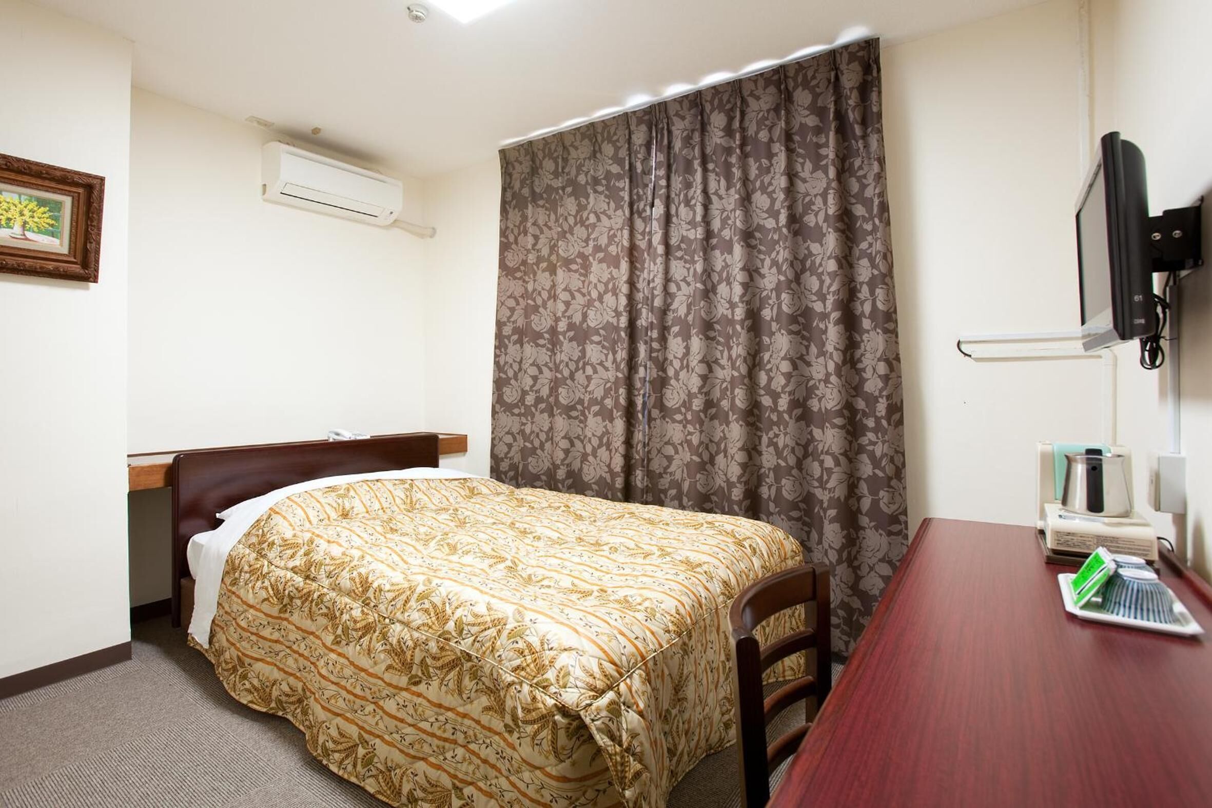 A hotel room with a bed, a desk, a chair, an air conditioner, a television, and a curtain.