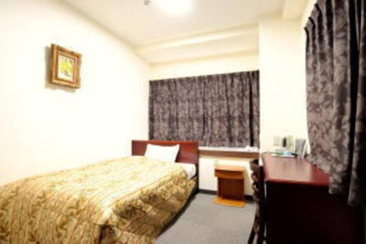 A hotel room with a bed, a desk, a chair, a window with curtains, and a framed picture on the wall.