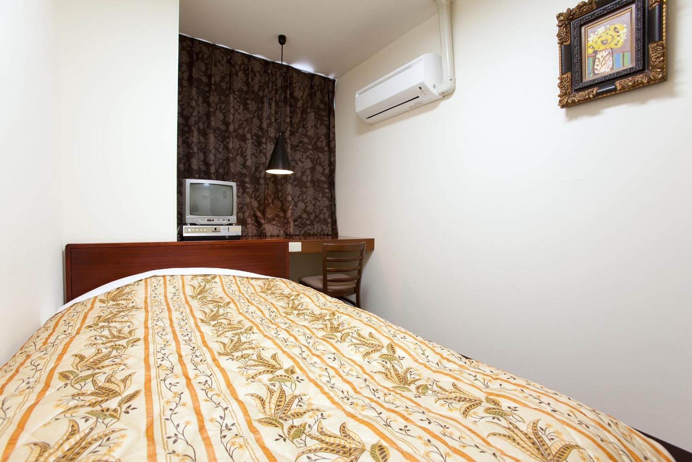 Een slaapkamer met een bed, bureau, stoel, televisie en airconditioning.
