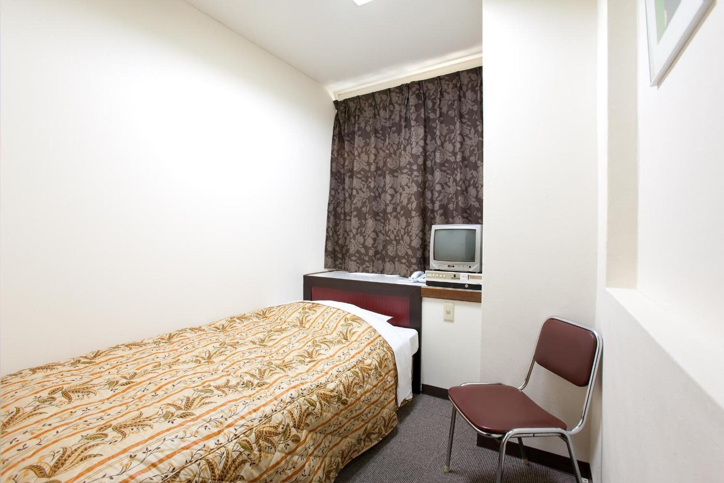 Une chambre d’hôtel avec un lit, un bureau avec une télévision et une chaise.