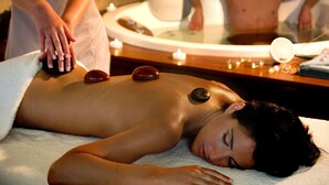 A person receiving a hot stone massage with a therapist's hands on their back.