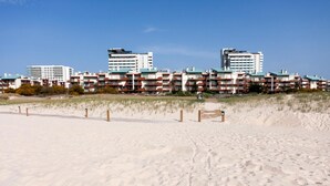 Un hotel sulla spiaggia con edifici a più piani, una spiaggia sabbiosa in primo piano e un cielo azzurro limpido.