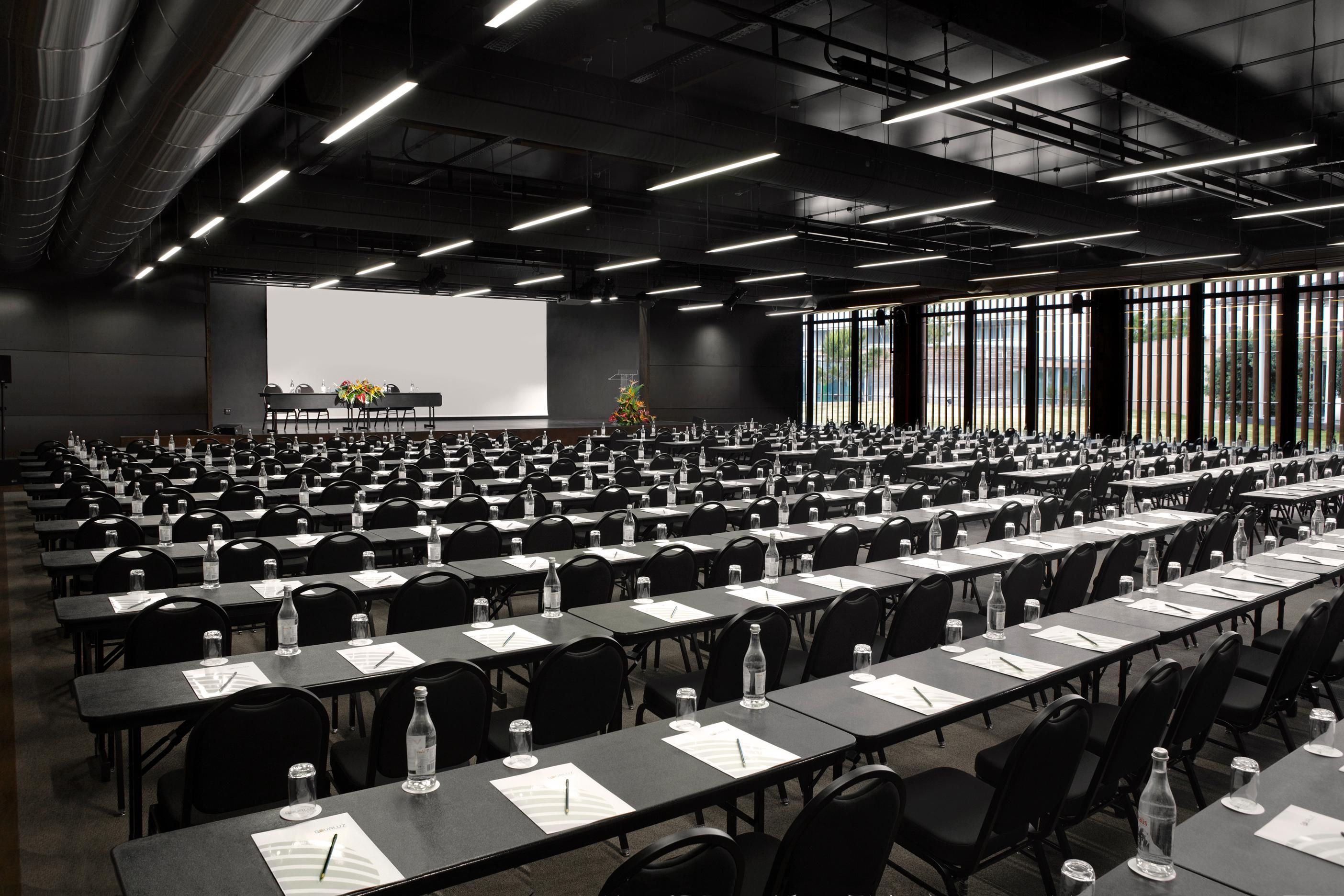 A conference room with rows of tables, chairs, and a large screen for presentations.