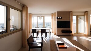 A modern living room with a dining area, large windows, and a flat-screen TV.