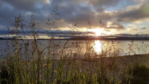 A lakeside view with tall grasses in the foreground and a sunset over the water. - Lakefront Resort (Rotorua)