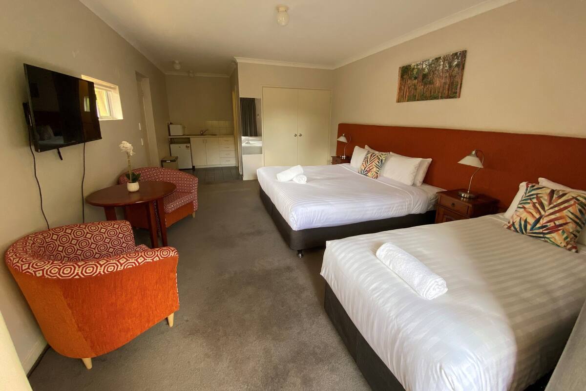A hotel room with two beds, a TV, a small dining table, and a sofa.
