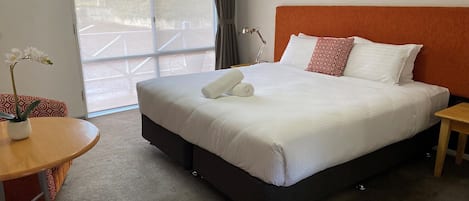 Une chambre d’hôtel avec un grand lit, une table ronde en bois, une orchidée en pot et une vue sur l’extérieur grâce à une porte coulissante.