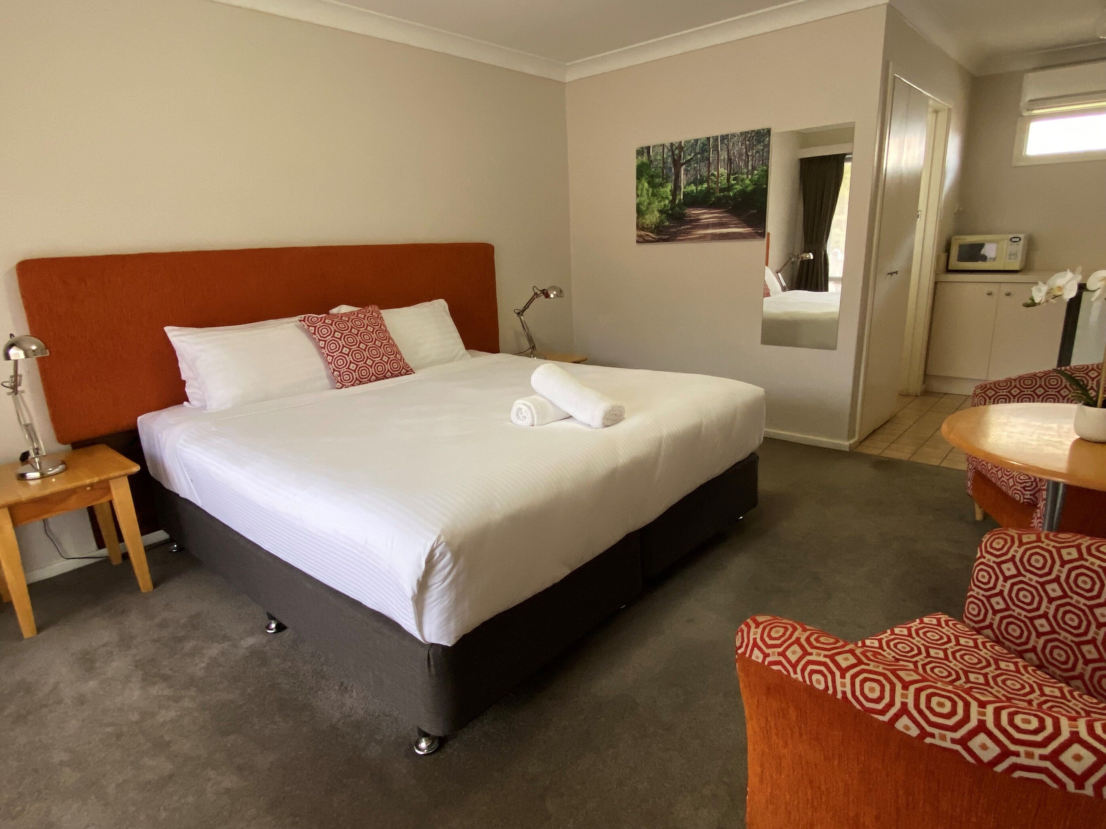 Une chambre d’hôtel avec un grand lit, une table de chevet avec une lampe, une chaise et une petite table sur laquelle est posé un vase de fleurs.