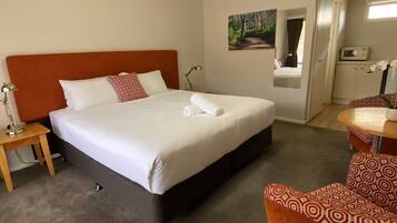 A hotel room with a large bed, a bedside table with a lamp, a chair, and a small table with a vase of flowers.