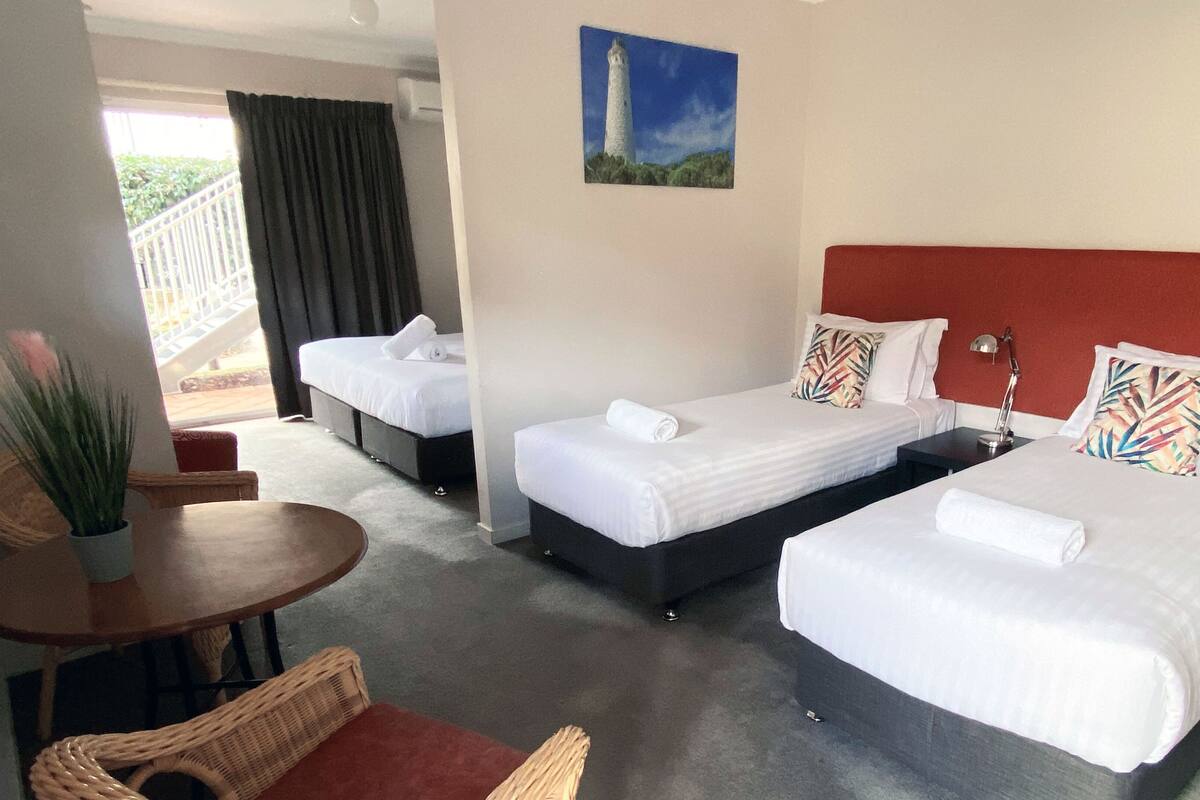 A hotel room with two beds, a small table, a chair, and a painting of a lighthouse.