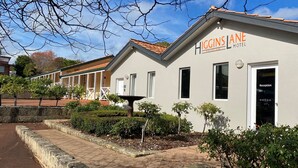 Un edificio de dos pisos con el nombre 'Higgins Lane Hotel' en la fachada. Cuenta con una recepción y puerta de vidrio, y un techo de tejas.