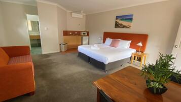 Ein Hotelzimmer mit Bett, Schreibtisch, Stuhl, kleinem Tisch, Mülleimer, Mikrowelle, Spüle und einer Zimmerpflanze.