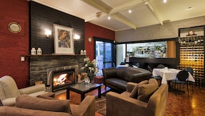 A cozy living room with a fireplace, leather sofas, and a bar area with wine bottles. - Burnie Airport Motel (Wynyard)