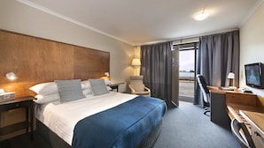 A hotel room with a large bed, a desk, a chair, a television, and a window with curtains. - Burnie Airport Motel (Wynyard)