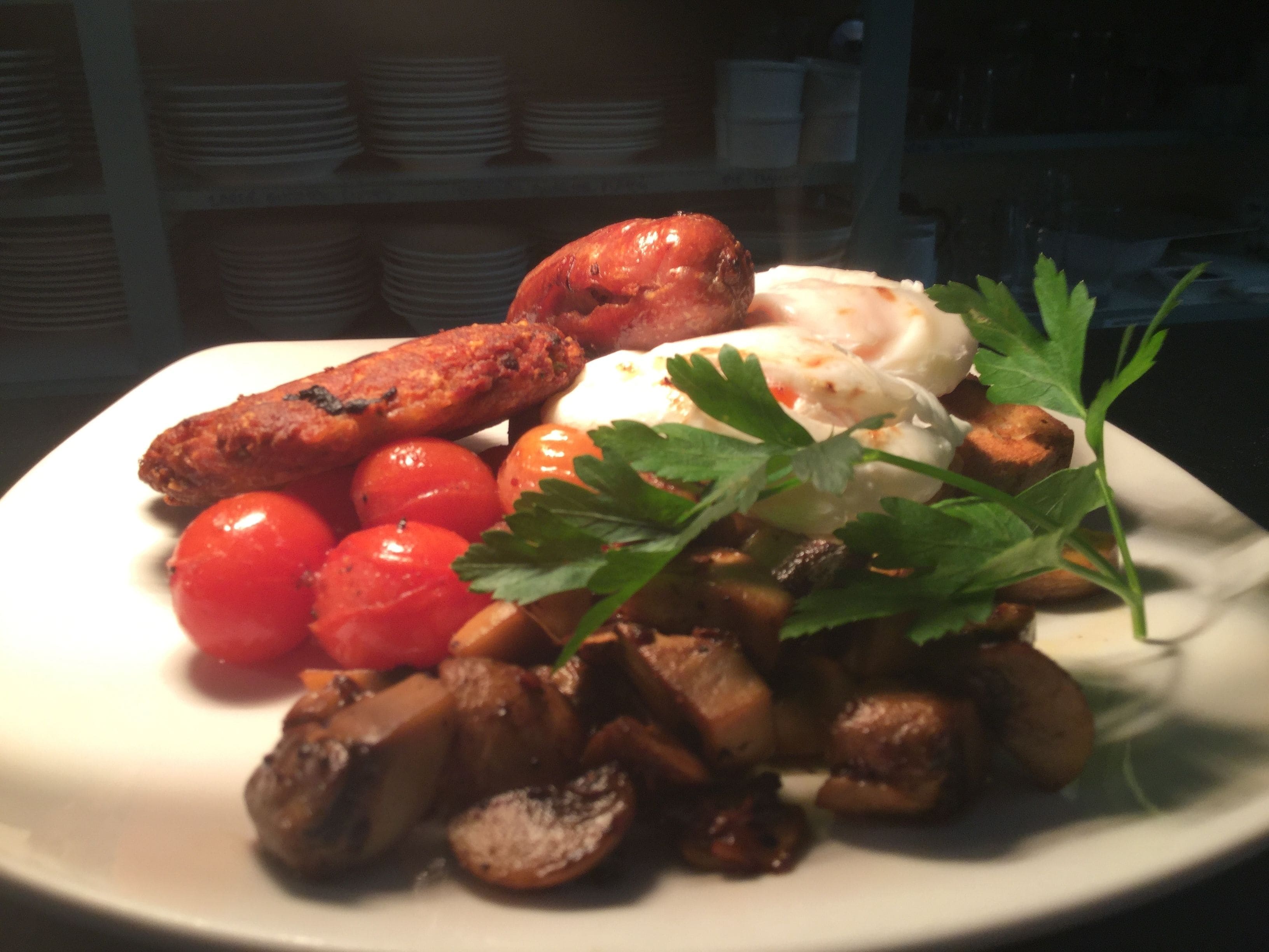 A plate of food with sausages, tomatoes, mushrooms, and a garnish.