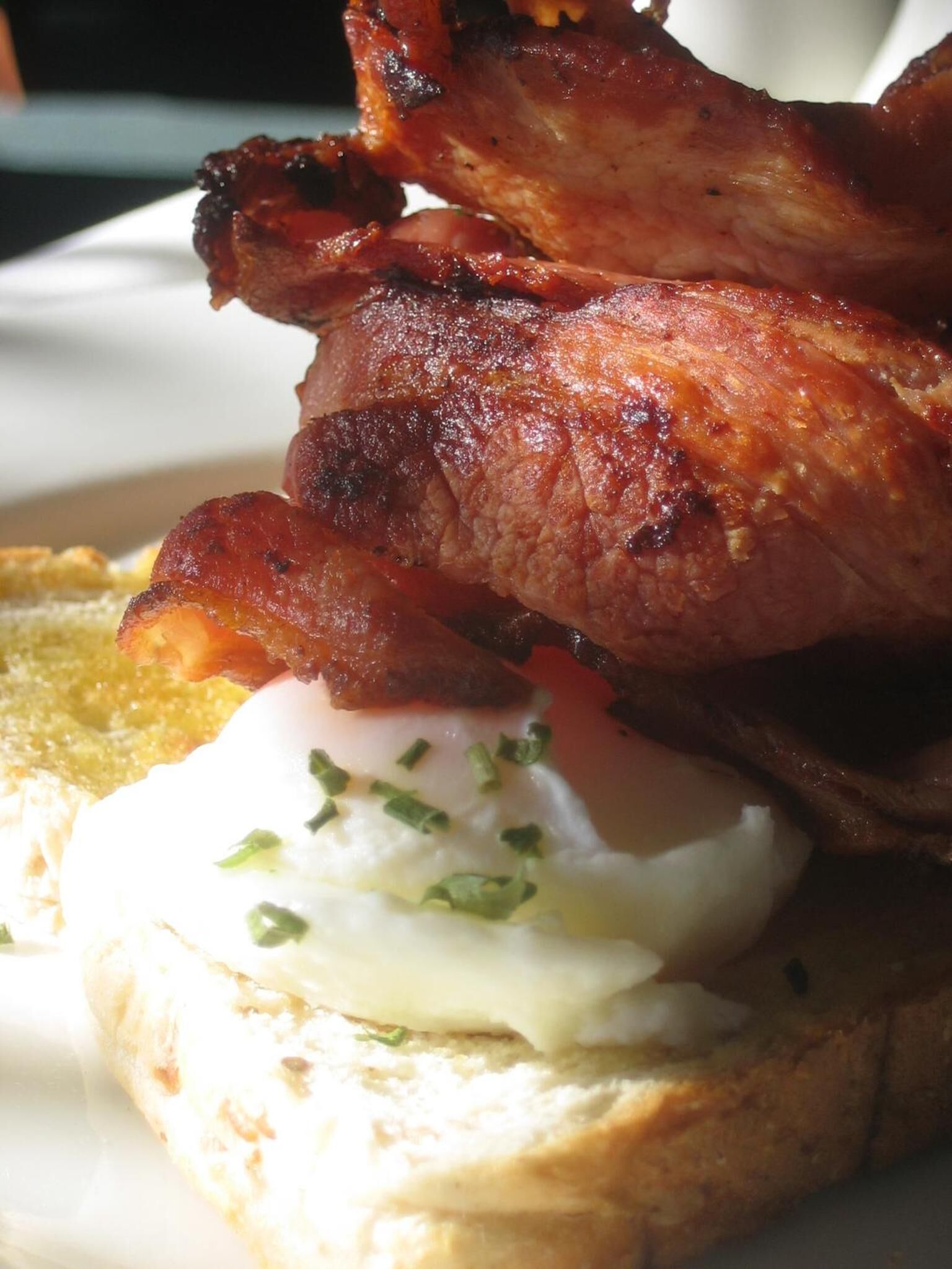 Une assiette de petit-déjeuner avec du bacon, un œuf poché et des toasts.