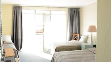 A hotel room with two beds, a small table, a lamp, and a view through a sliding door.