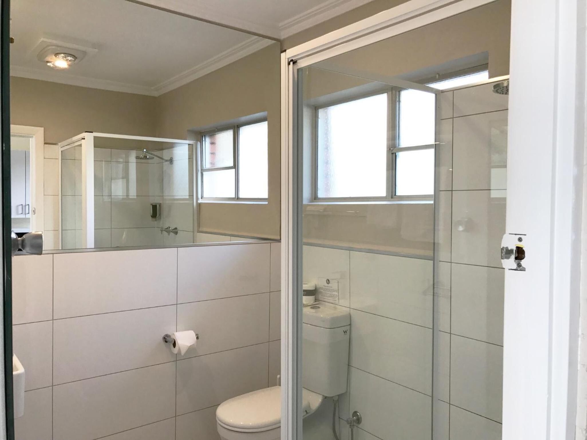 Moderni kylpyhuone, jossa on lasinen suihkuseinä, wc ja peili.