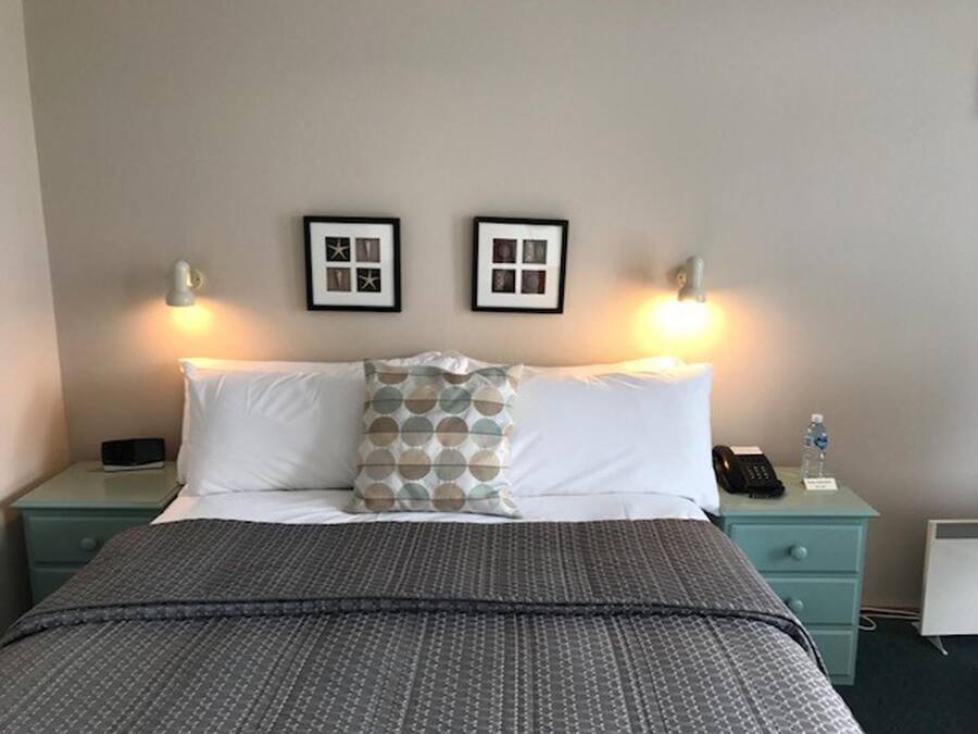 A hotel room with a bed, two bedside tables, a nightstand, a lamp, and two framed pictures on the wall.