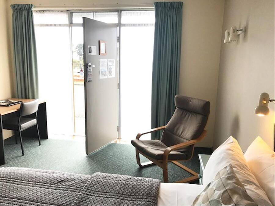 A hotel room with a bed, a desk, a chair, and a door leading to the outside.