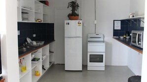 A compact kitchen with white appliances, a potted plant, and a microwave. - Tin Can Bay Budget Accommodation - Hostel (Tin Can Bay)