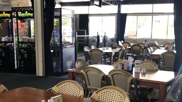A restaurant with wooden tables and wicker chairs, large windows, and a view of the street outside. - Tin Can Bay Budget Accommodation - Hostel (Tin Can Bay)