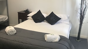 A hotel room with a bed, a nightstand, a painting on the wall, and a tall plant. - Tin Can Bay Budget Accommodation - Hostel (Tin Can Bay)