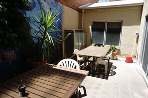 A patio area with a wooden table and chairs, a potted plant, and a mural on the wall. - The Guesthouse - Hostel (Adelaide)