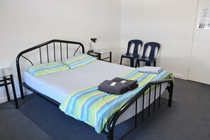 A single bed with a striped bedspread, a pair of chairs, a small table with a lamp, and a wall-mounted bulletin board. - The Guesthouse - Hostel (Adelaide)