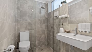 A modern bathroom with a glass-enclosed shower, a toilet, and a sink with hand soap dispensers.