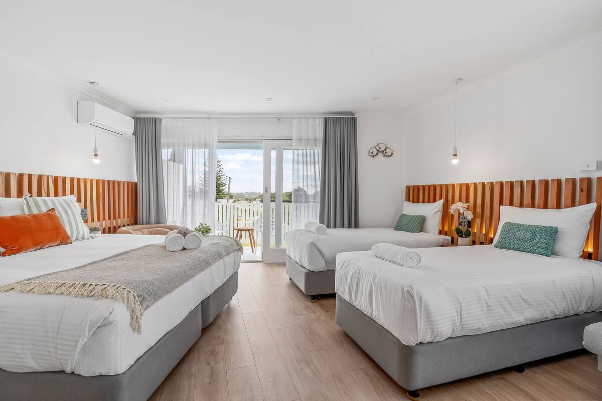 A hotel room with two beds, a balcony, and a view of greenery.