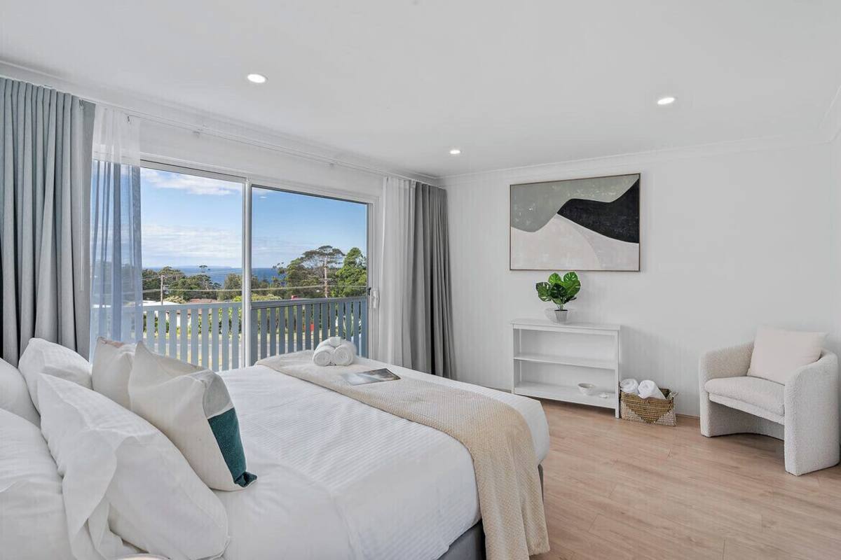 A modern hotel room with a large bed, a view of the outdoors, a white console table, and a chair.