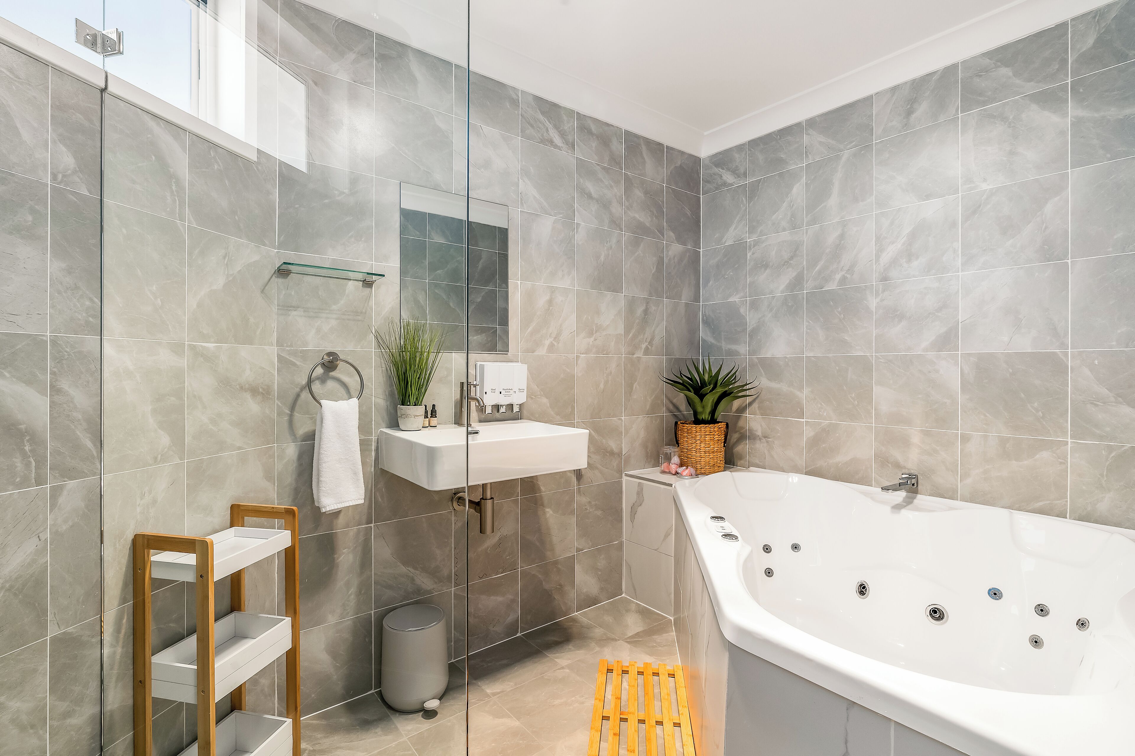 Ein modernes Badezimmer mit einer großen Badewanne, einer Glasablage und einem Spiegel.