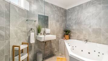 A modern bathroom with a large bathtub, a glass shelf, and a mirror.