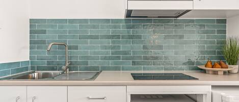 A kitchen with white cabinets, a stainless steel sink, a microwave, and a green tiled backsplash.