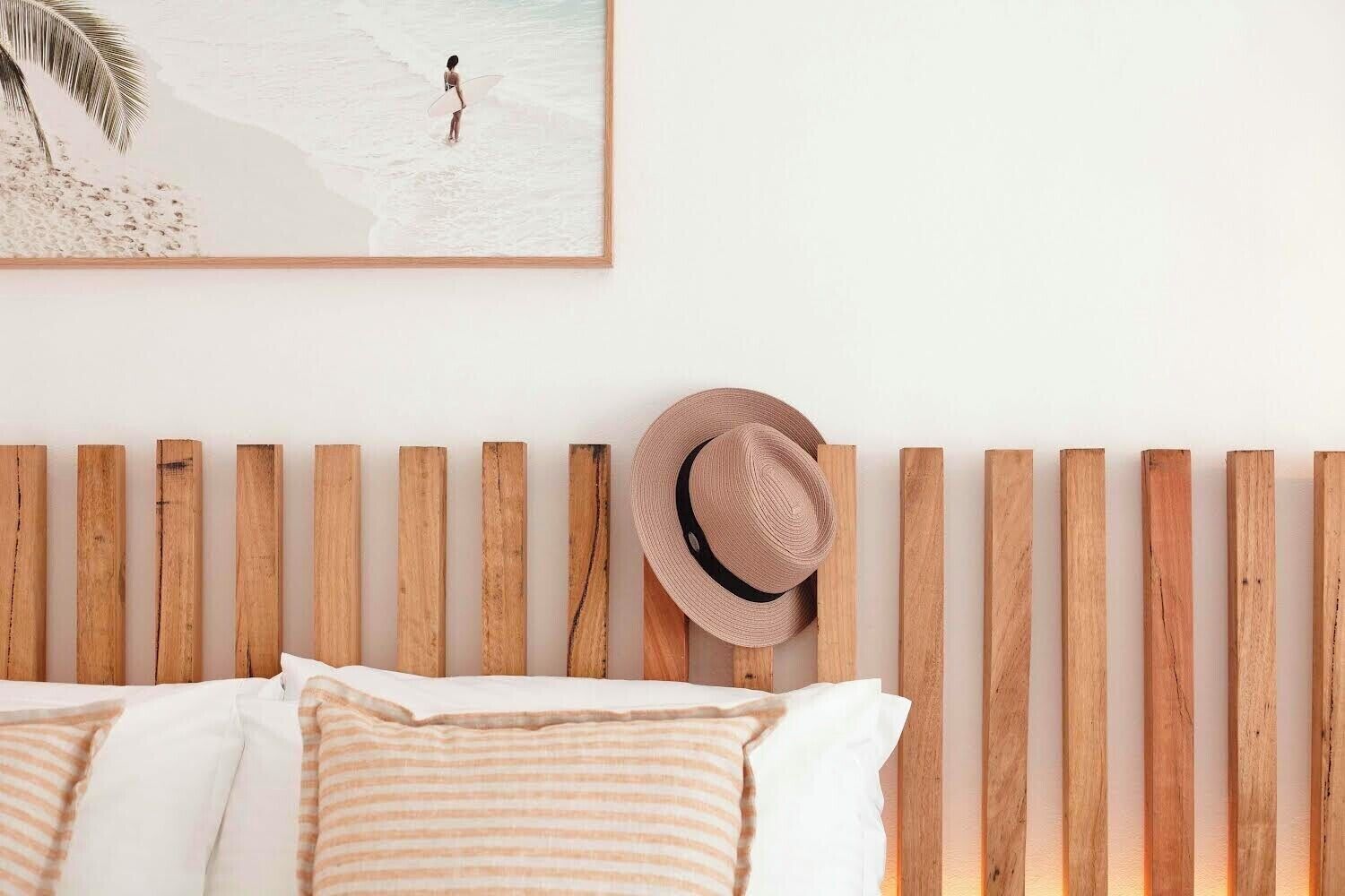 A bedroom with a wooden headboard, a beach-themed painting, and a straw hat.