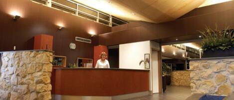 Un espace d’accueil avec un comptoir en pierre, une réceptionniste et un espace piscine agrémenté d’un mur en pierre.