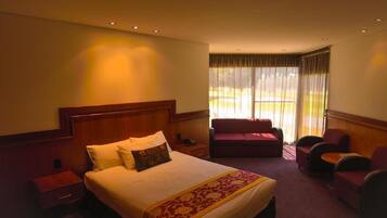 A hotel room with a large bed, a red sofa, a small table, and a view of the outdoors through sheer curtains.